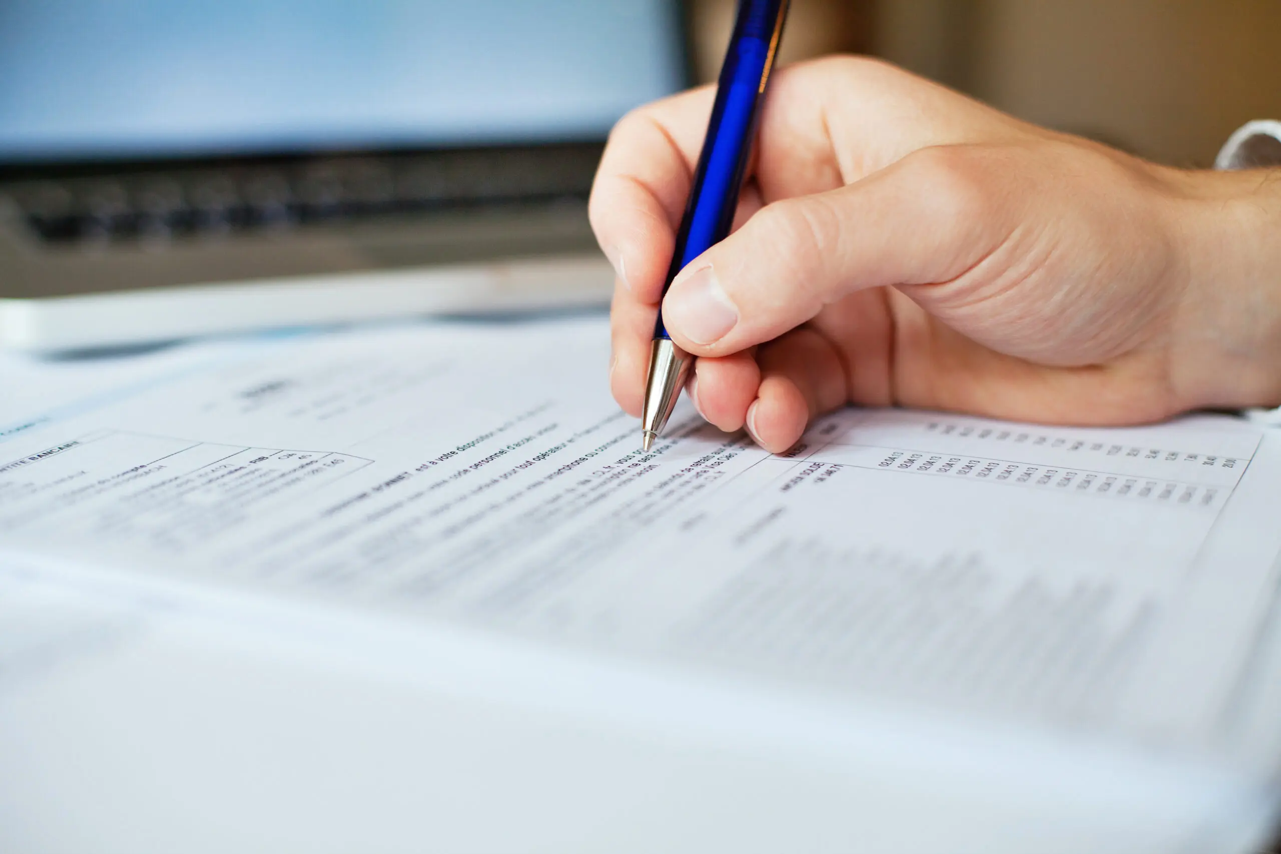 close-up of hand writing on document with blue pen