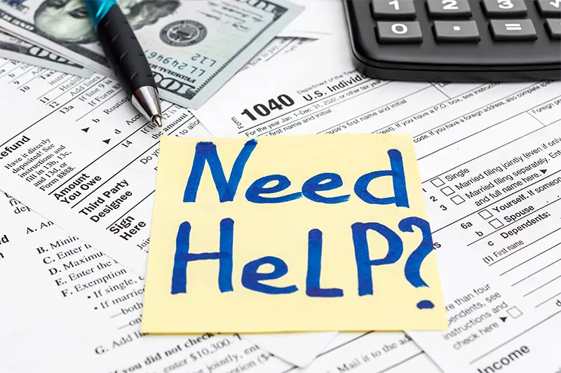 Post it with the words Need Help? written in blue on top of tax documents